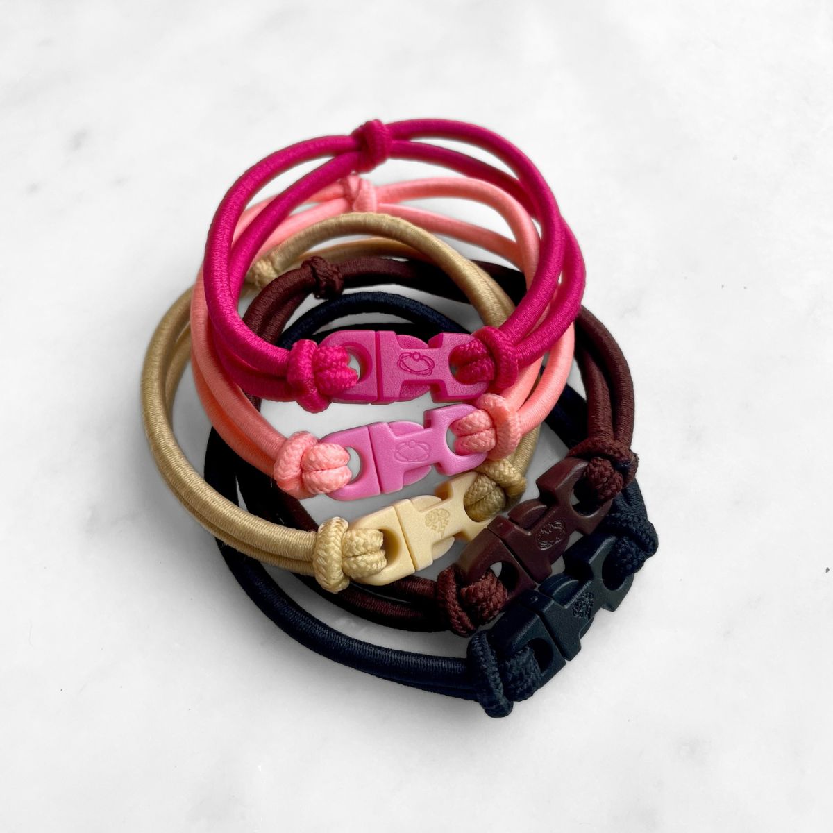 Close view of a variety stack of Buckle Hair Ties showing the pink, blonde, brown, and black buckles