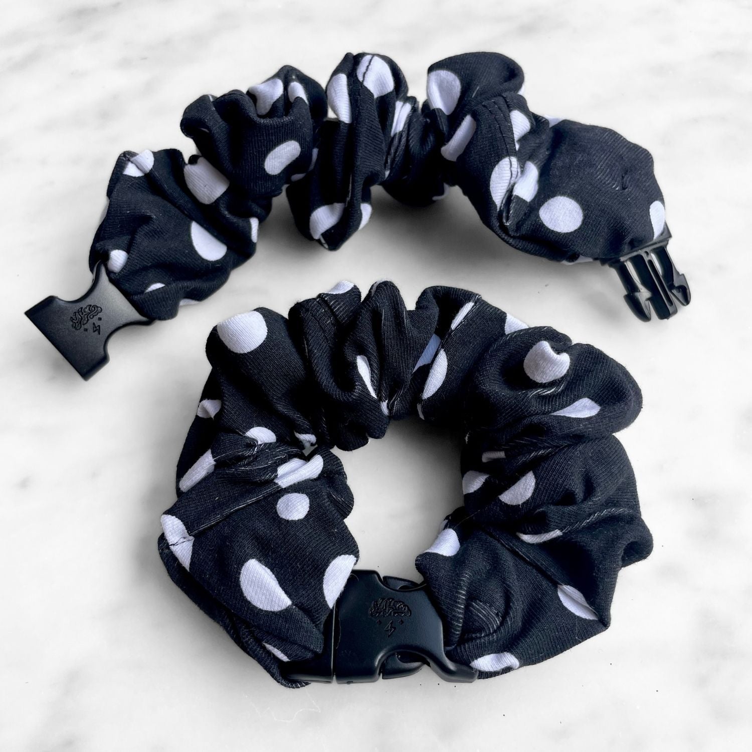 Black and white polka dot Buckle Scrunchie with a black quick-release buckle on marble