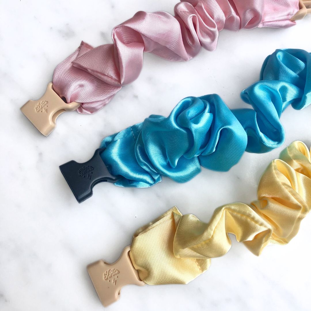 Three pastel Buckle Scrunchies in pink, blue, and yellow recycled satin