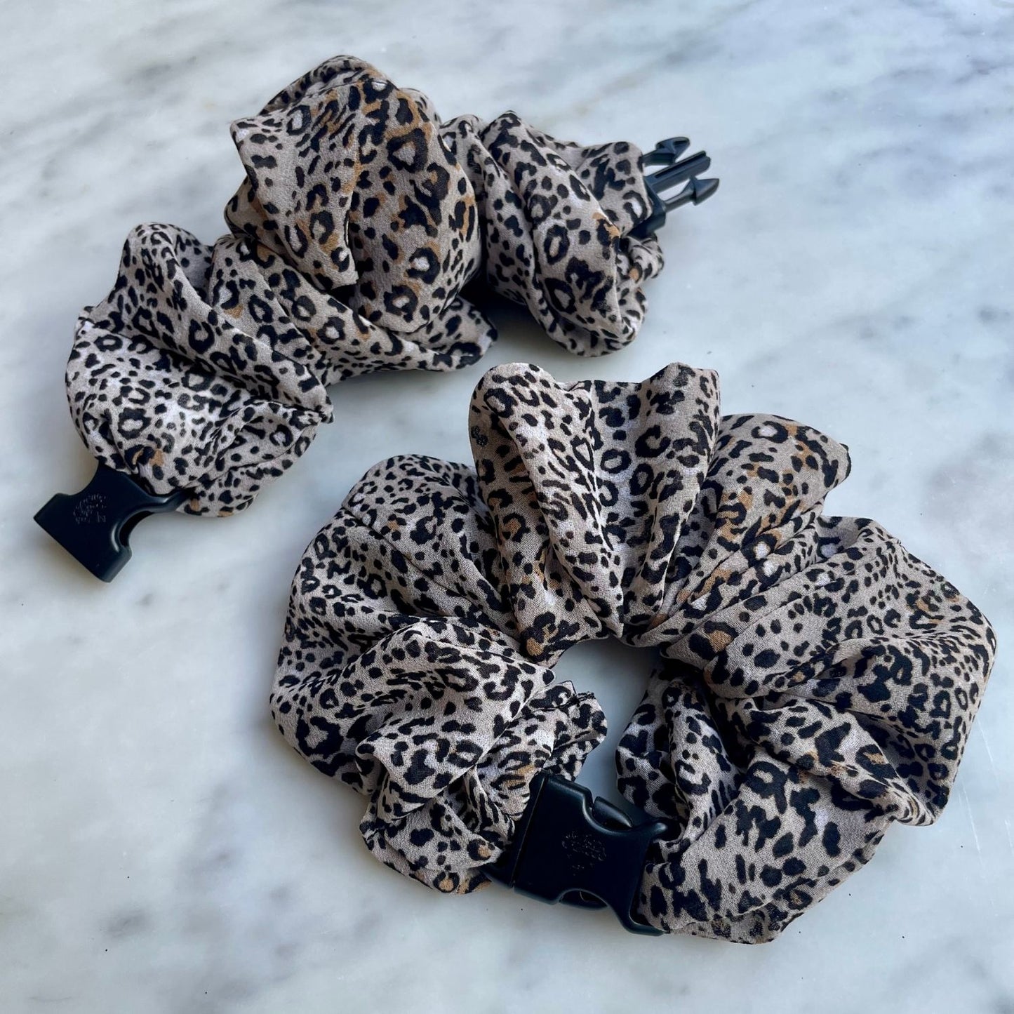 Leopard print chiffon Buckle Scrunchie with a navy quick-release buckle on marble