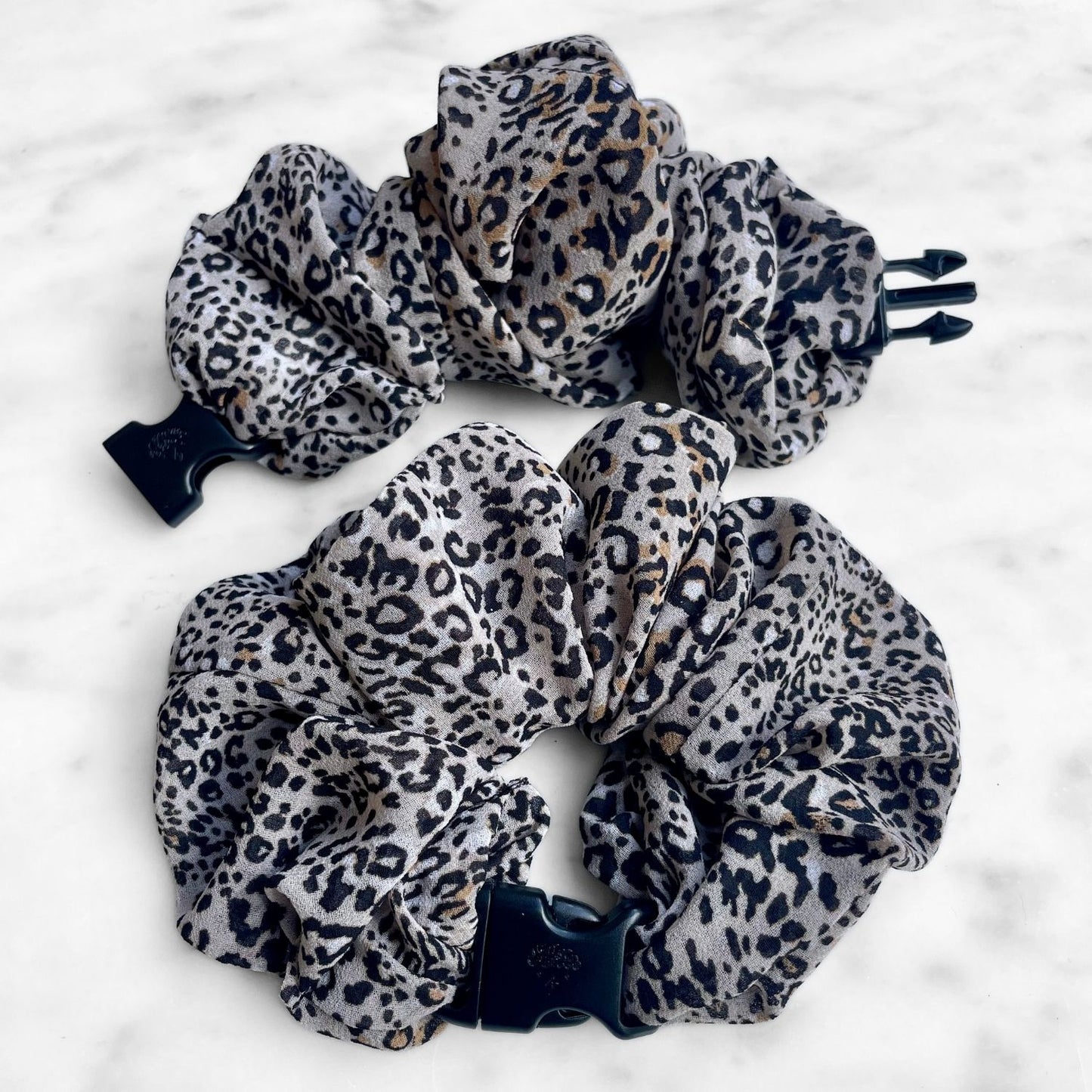 Two leopard print chiffon Buckle Scrunchies, one open showing the navy buckle prongs
