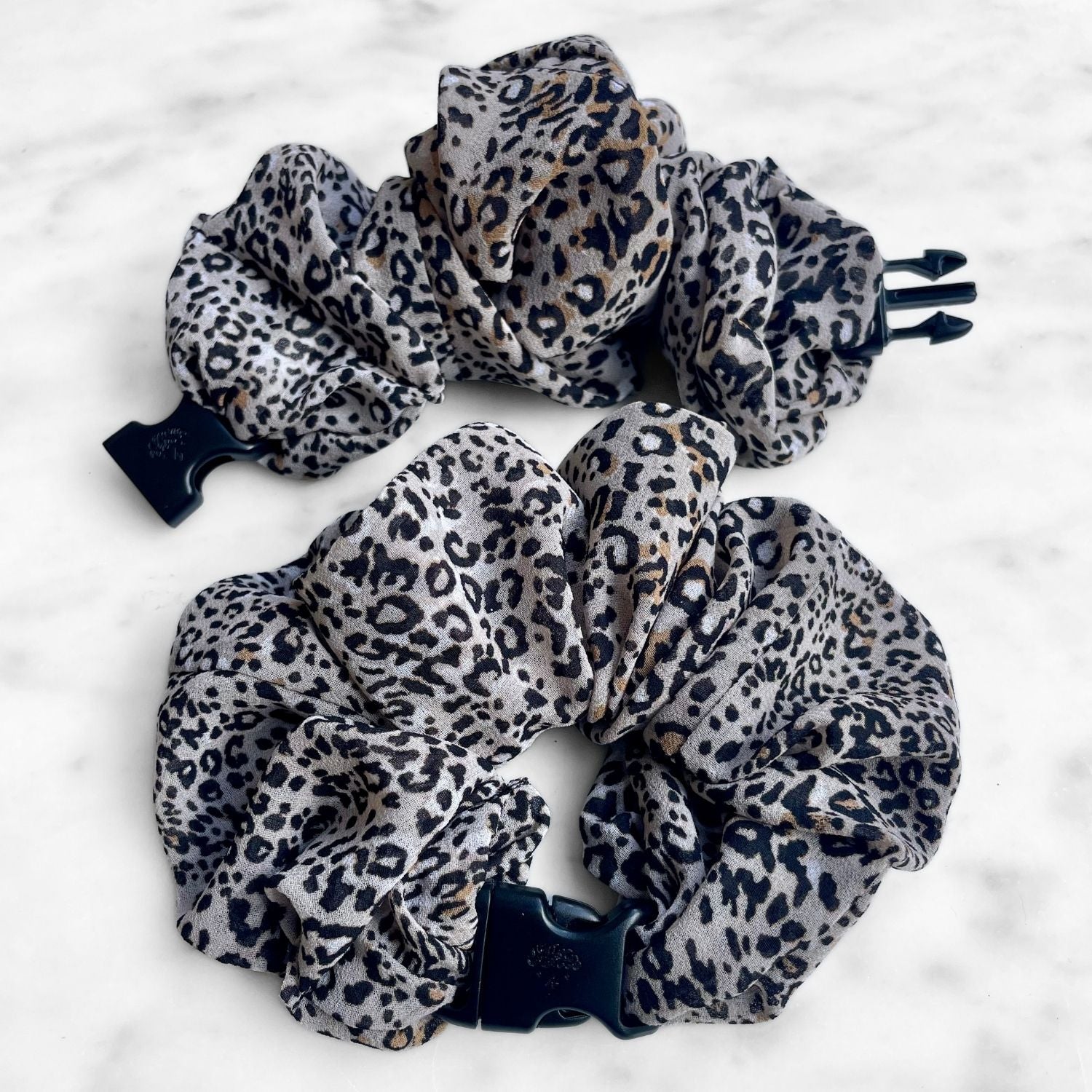 Two leopard print chiffon Buckle Scrunchies, one open showing the navy buckle prongs