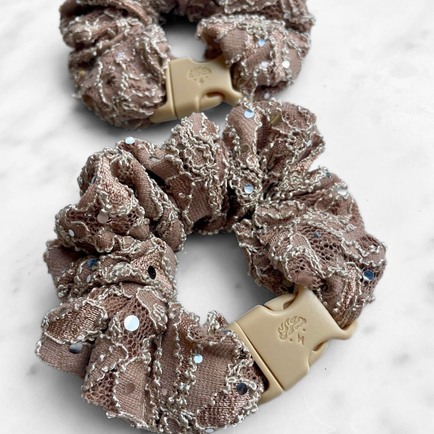 Overhead view of a mauve rhinestone lace Buckle Scrunchie and its tan buckle