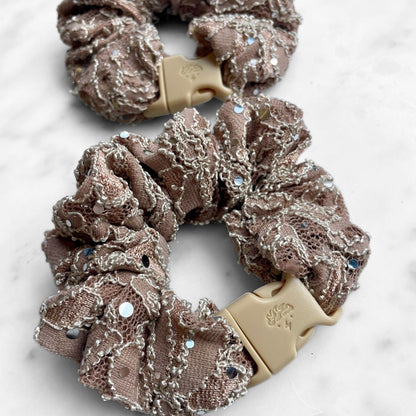 Overhead view of a mauve rhinestone lace Buckle Scrunchie and its tan buckle
