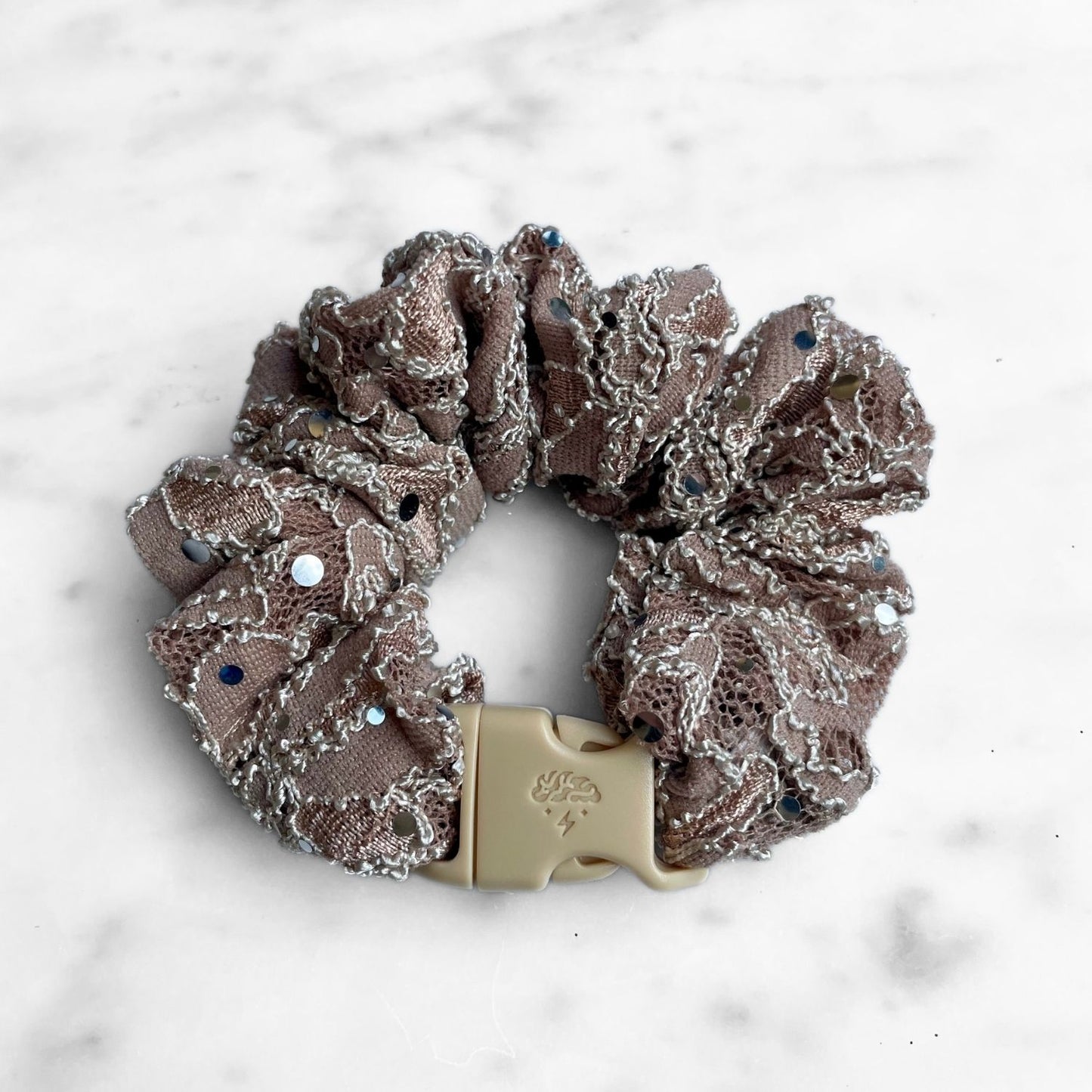 Mauve lace Buckle Scrunchie with blue rhinestones fastened in a ring on marble
