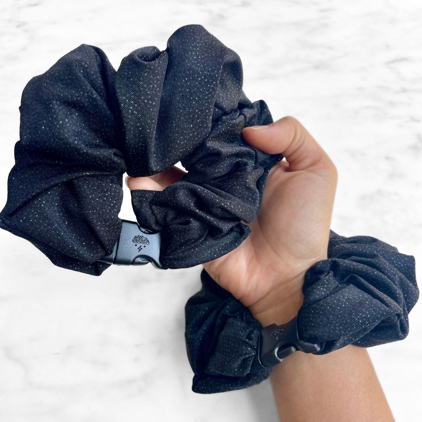 Black glitter Buckle Scrunchie held in hand with a second worn on the wrist
