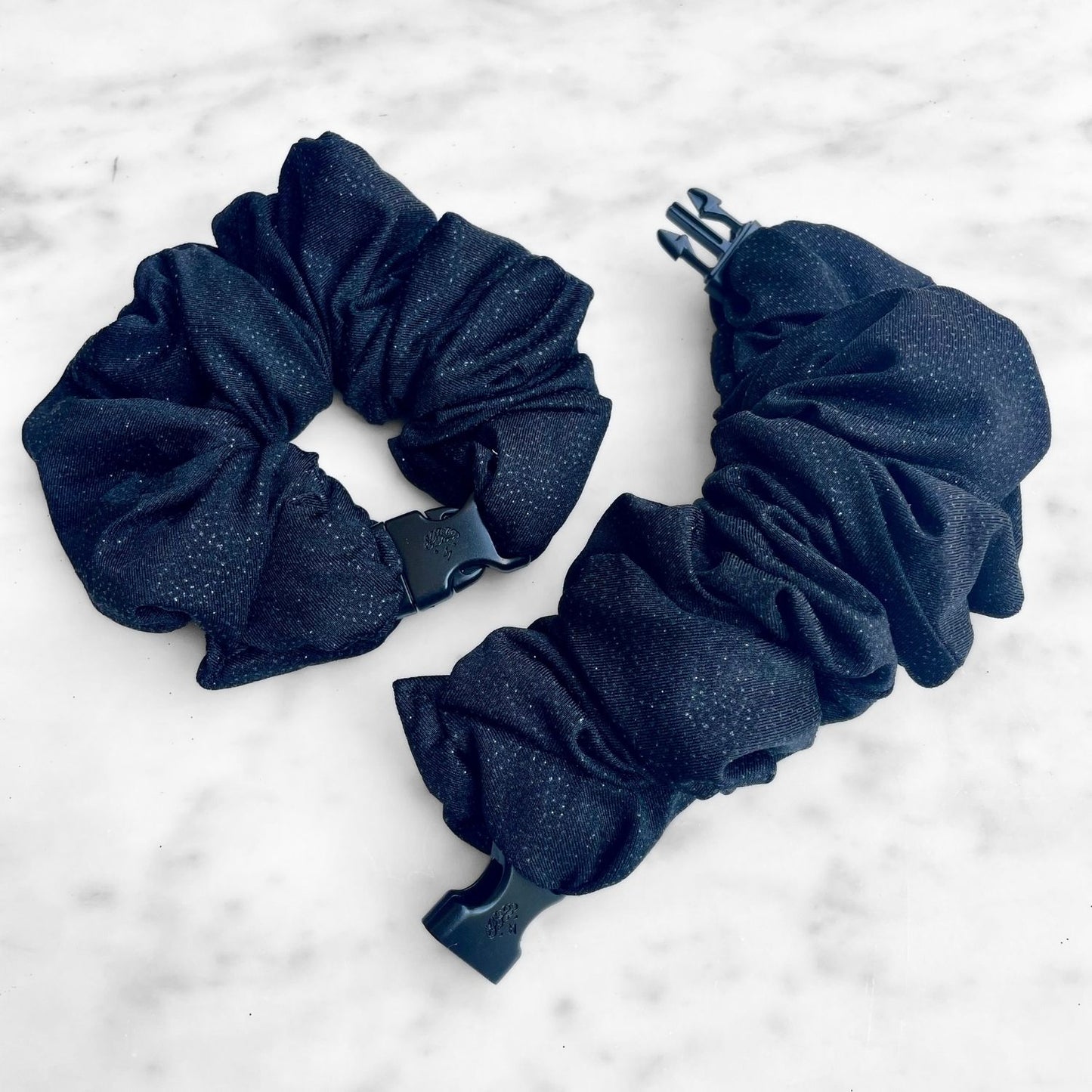 Two black glitter Buckle Scrunchies laid open on white marble