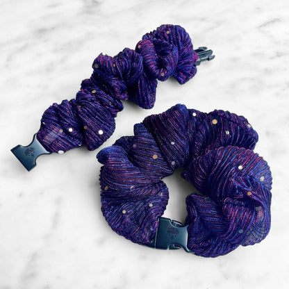 Two purple pleated sparkle Buckle Scrunchies on marble, one unclipped