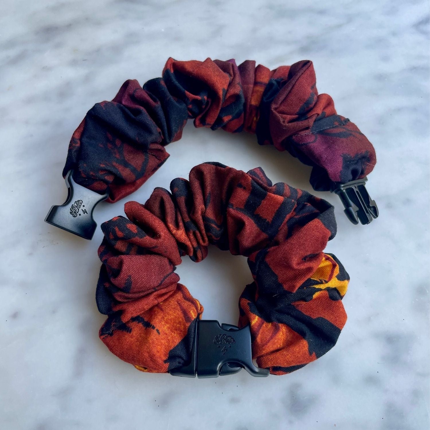 Two red and orange abstract print Buckle Scrunchies on white marble