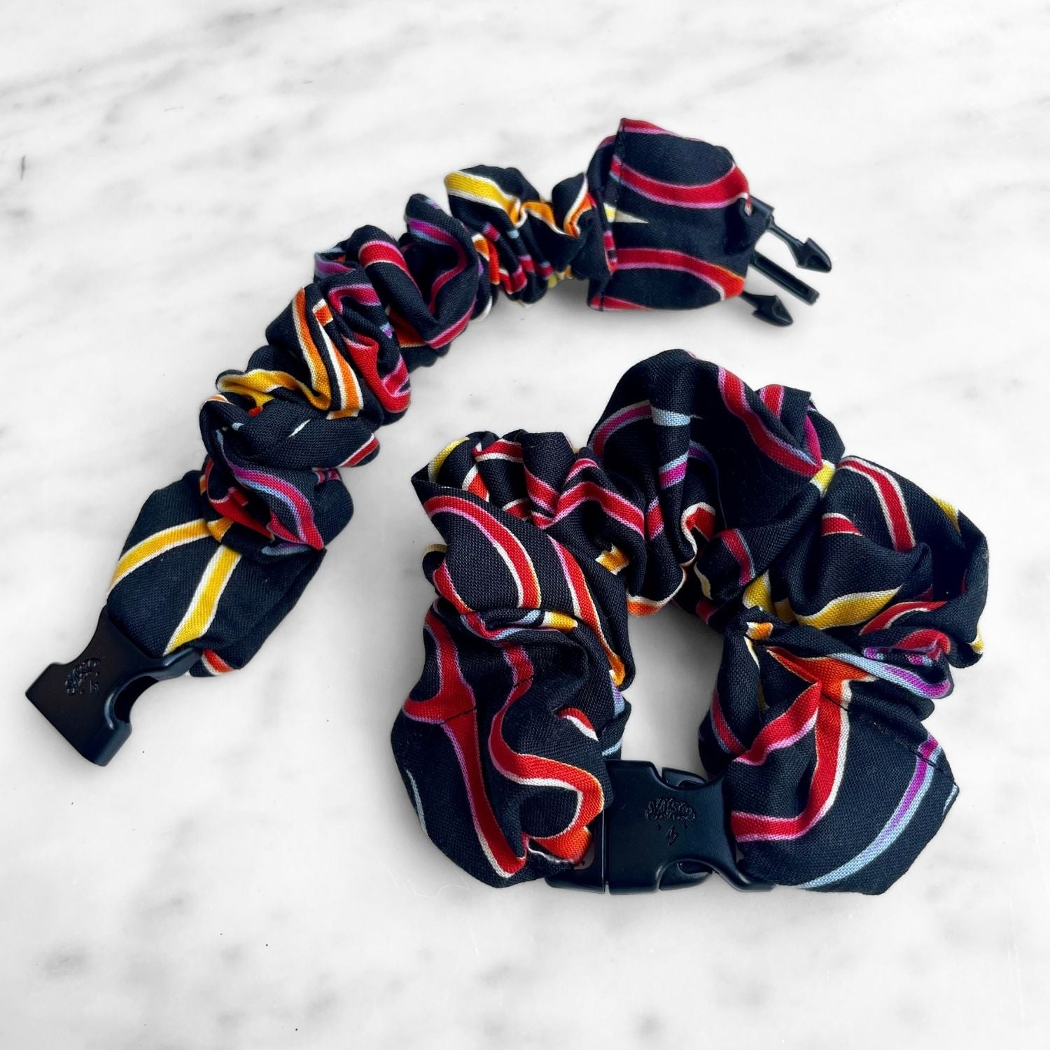 Black Buckle Scrunchie with red, yellow, and pink ribbon swirl stripes on marble