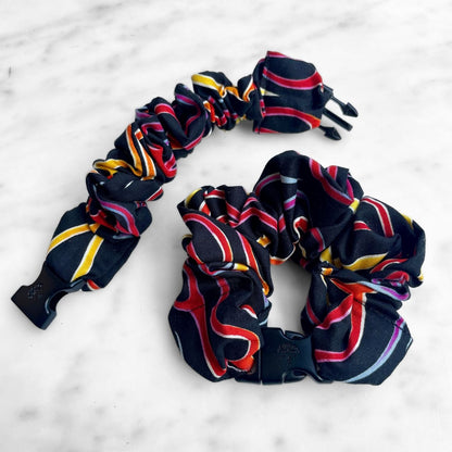 Black Buckle Scrunchie with red, yellow, and pink ribbon swirl stripes on marble