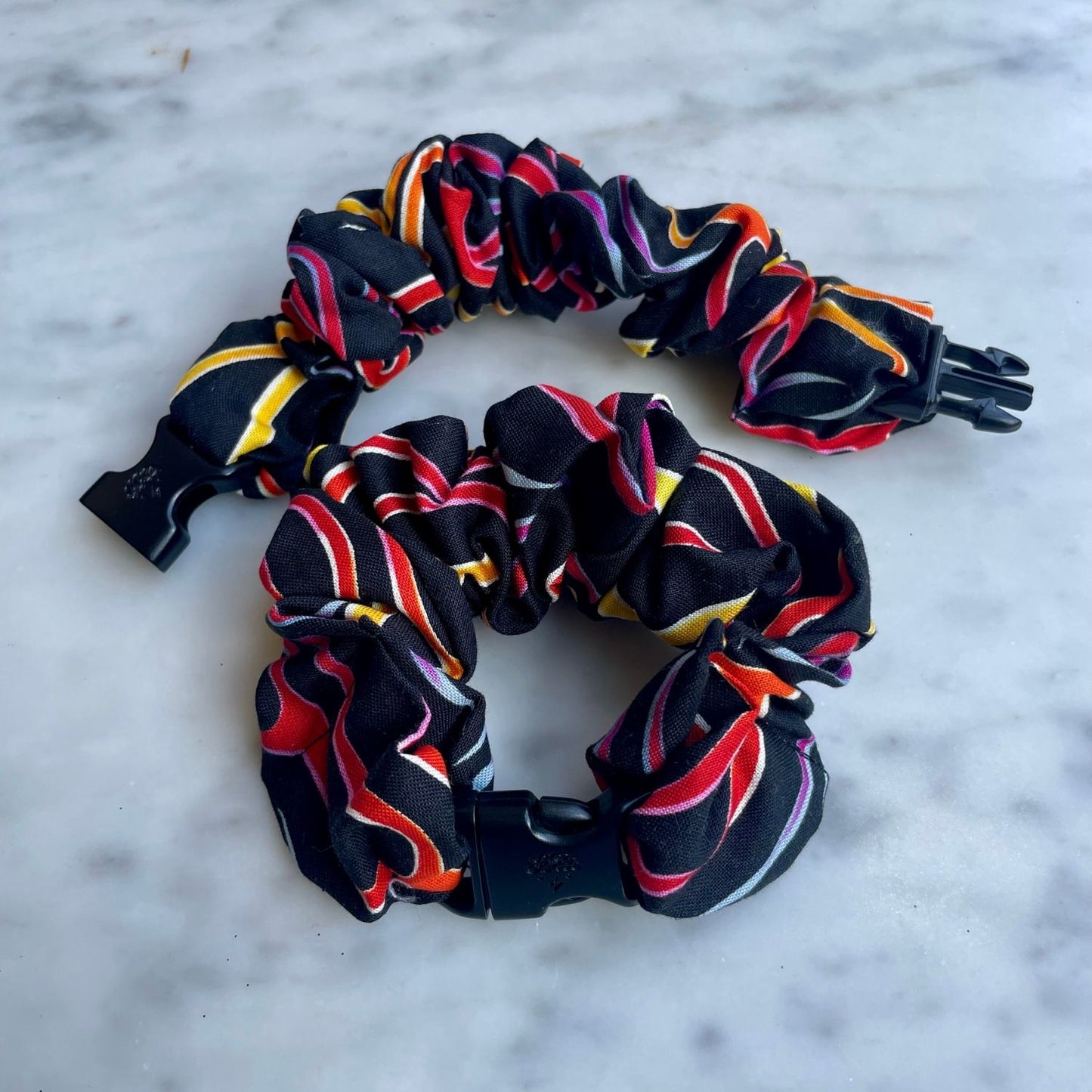 Two black ribbon swirl print Buckle Scrunchies, one open with the buckle unclipped