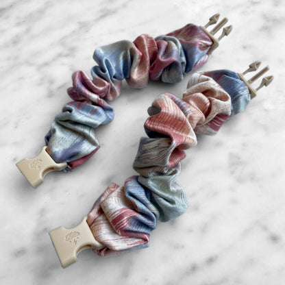 Two pink and blue watercolor Buckle Scrunchies laid open on marble with tan buckles